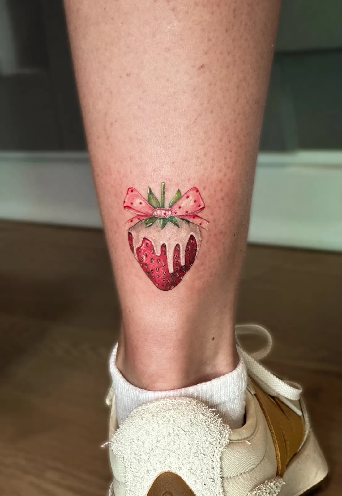 Tatuaj color pe gambă cu o căpșună înmuiată în ciocolată albă și o fundă roz