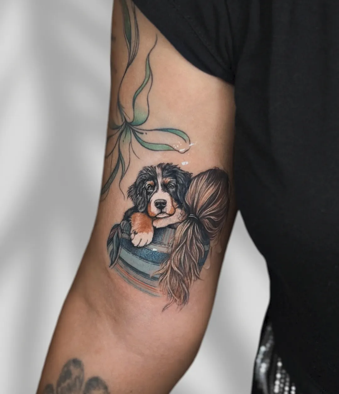 Tatuaj color pe braț cu un cățeluș bernez într-o găleată și o fundă