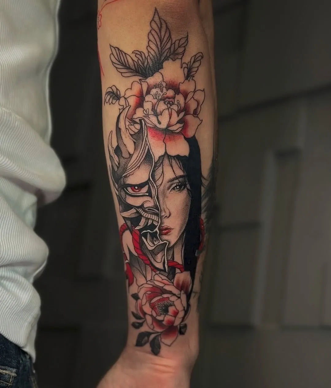 Tatuaj neo-tradițional pe antebraț cu o femeie, o mască oni și bujori în roșu și negru