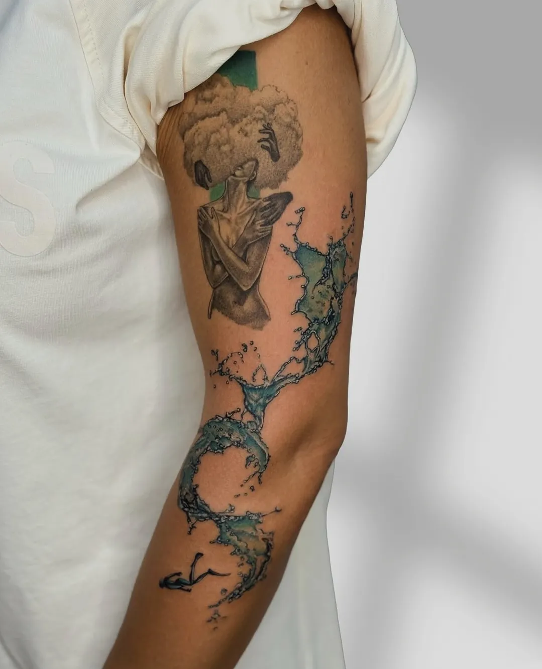Tatuaj color pe braț cu o femeie cu părul din nori și un val de apă