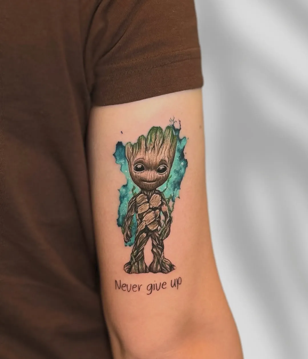 Tatuaj color pe braț cu Baby Groot și textul Never give up