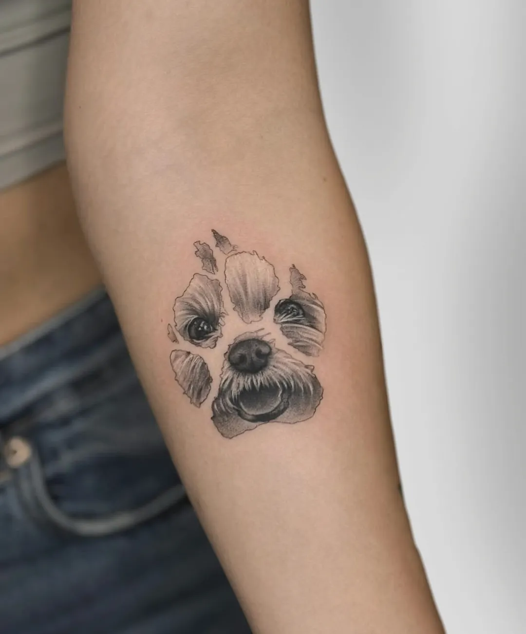 Tatuaj alb-negru pe braț cu o labă de câine cu chipul cățelului în interior