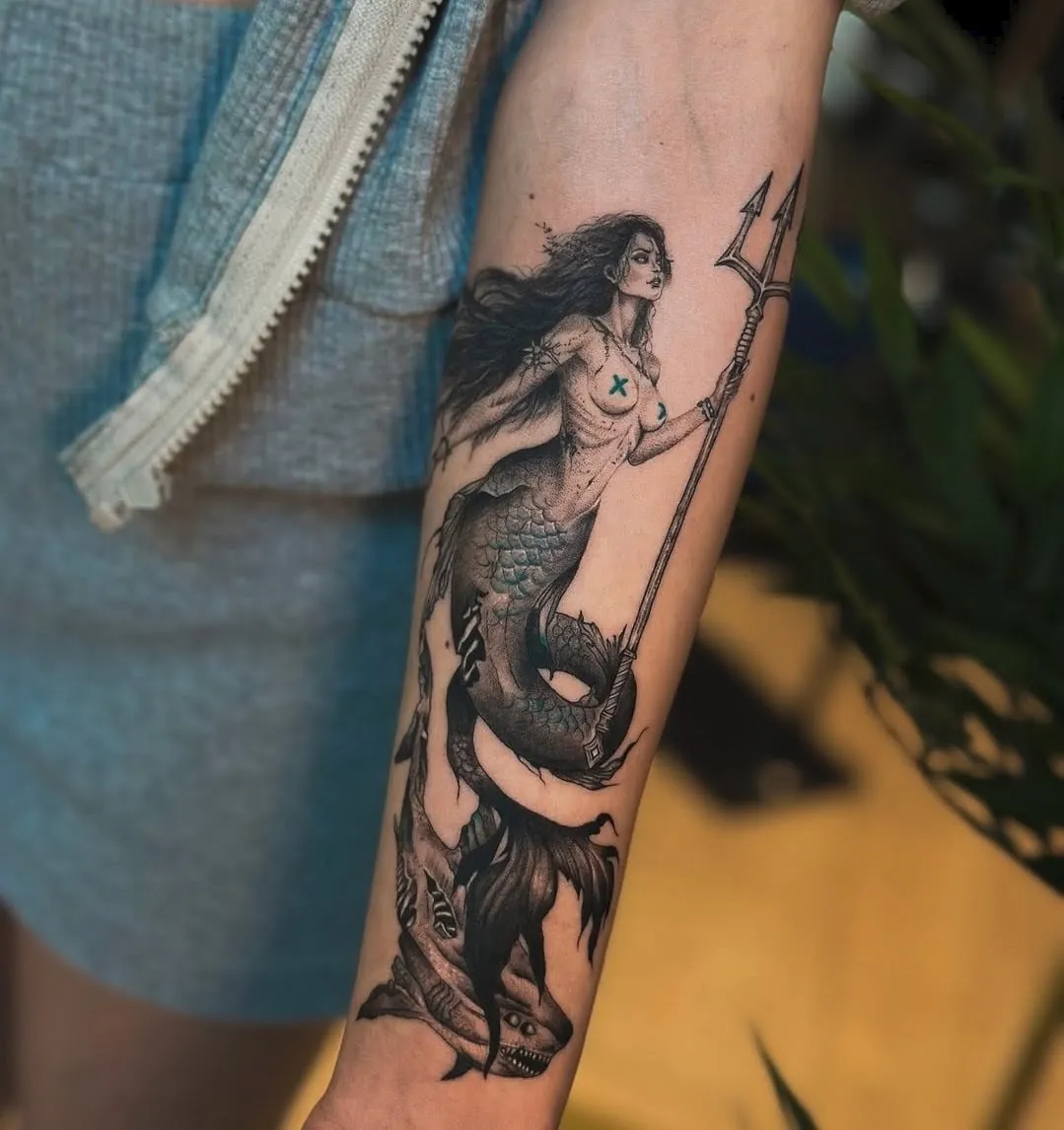 Tatuaj alb-negru pe antebraț cu o sirenă cu trident și un rechin